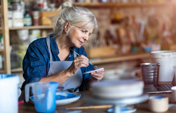 A senior woman carefully painting a ceramic bowl with paint